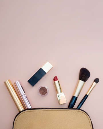 Top view of cosmetics standing out from beige makeup bag on pink background. photoの写真素材