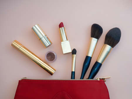 Top view of cosmetics standing out from red cosmetic bag on pink background. photoの写真素材
