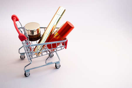 Front view of a shopping cart with makeup products on a pink background. Cosmetic shopping concept. photoの写真素材