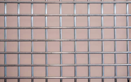 Metal chrome grate with a square mesh on a pink background.の写真素材