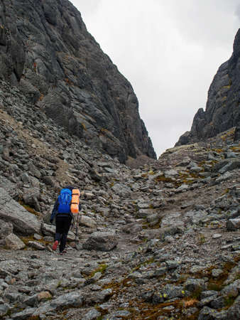 A young woman tourist with a backpack goes through a lifeless rocky pass.の写真素材