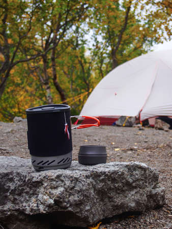 A pot for a gas burner with a mug sits on a stone against the background of a tent. photoの写真素材