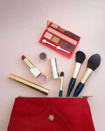Top view of cosmetics standing out from red cosmetic bag on pink background. photoの写真素材
