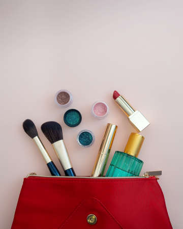 Top view of cosmetics standing out from red cosmetic bag on pink background. photoの写真素材