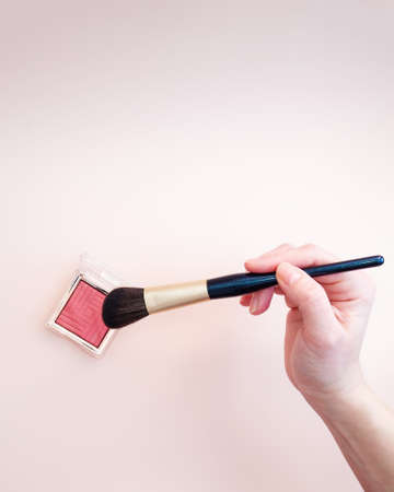 A golden makeup brush is dipped in blush on a pink background. photoの写真素材