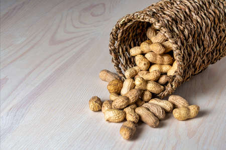 Shelled peanuts in a small wicker basket on a white background. Peanuts full from a wicker basket. Peanuts spill out of a wicker basket. photoの写真素材
