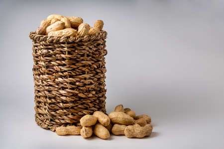 Shelled peanuts in a small wicker basket on a white background. Peanuts full from a wicker basket. Peanuts spill out of a wicker basket. photoの写真素材