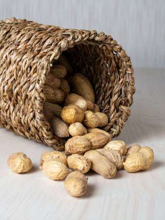 Shelled peanuts in a small wicker basket on a white background. Peanuts full from a wicker basket. Peanuts spill out of a wicker basket. photoの写真素材