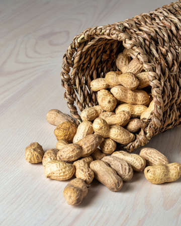 Shelled peanuts in a small wicker basket on a white background. Peanuts full from a wicker basket. Peanuts spill out of a wicker basket. photoの写真素材
