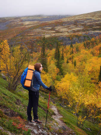 A young woman with a backpack and trekking poles in the Khibiny mountains. The concept of a healthy and active lifestyle. Girl on the background of nature mountains. photoの写真素材