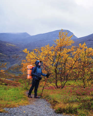 A woman with a backpack in the autumn season walks along a path in the mountains on a rainy day. photoの写真素材