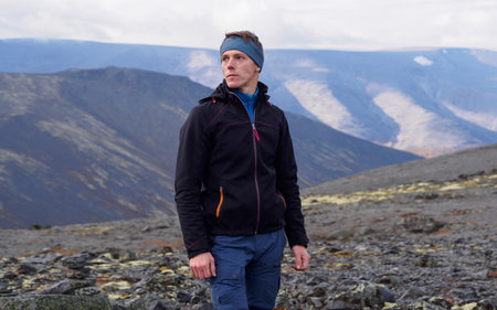 a young man with trekking poles in a bandana stands against the backdrop of mountains. photoの写真素材