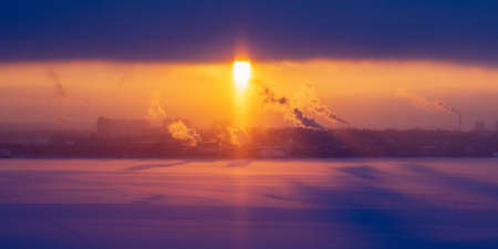 Chimneys of a factory with smoke and steam on a red sunset in the backgroundの写真素材