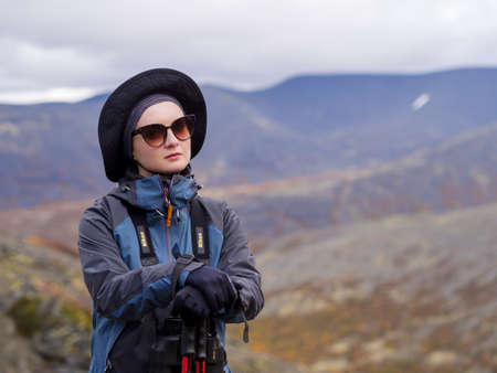 Young woman mountain tourist in glasses with trekking poles on the background of mountains.の写真素材