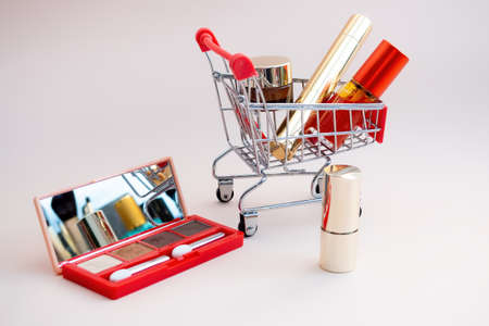 Front view of a shopping cart with makeup products on a pink background. Cosmetic shopping concept. photoの写真素材