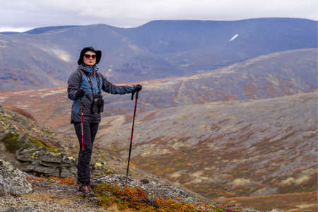 Young woman mountain tourist in glasses with trekking poles on the background of mountainsの写真素材