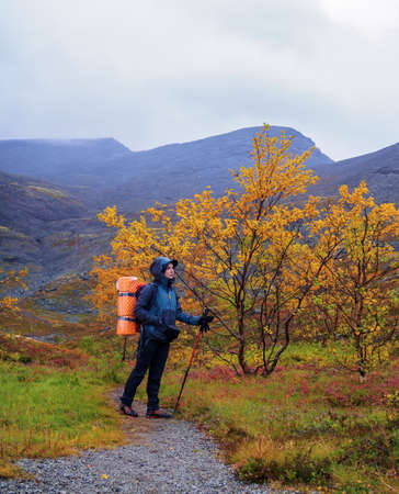 A woman with a backpack in the autumn season walks along a path in the mountains on a rainy day.の写真素材