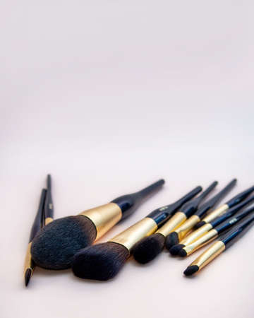 Assortment of female make-up of various face brushes. A set of professional dark blue and golden makeup brushes on a pink background. photoの写真素材