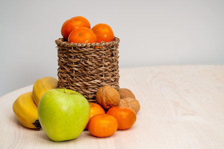 A variety of fruits and nuts on a wooden table. Tangerines in a wicker basket, bananas, apples and walnuts. photoの写真素材