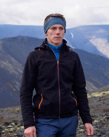 a young man with trekking poles in a bandana stands against the backdrop of mountains. photoの写真素材