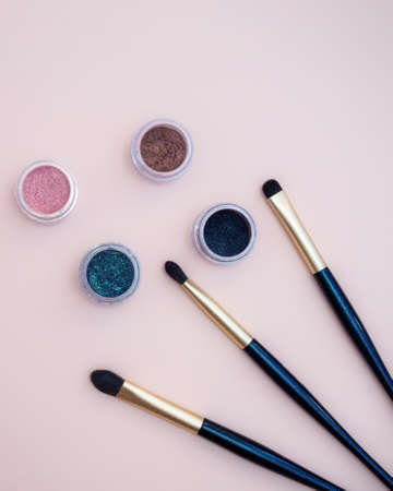 Composition with decorative makeup products golden brushes and colorful eye shadows on pastel pink background. photoの写真素材