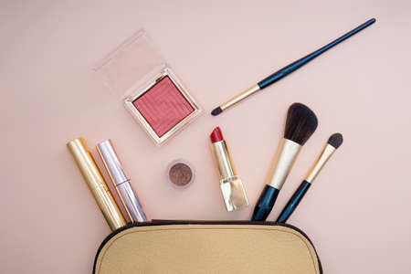 Top view of cosmetics standing out from beige makeup bag on pink background. photoの写真素材