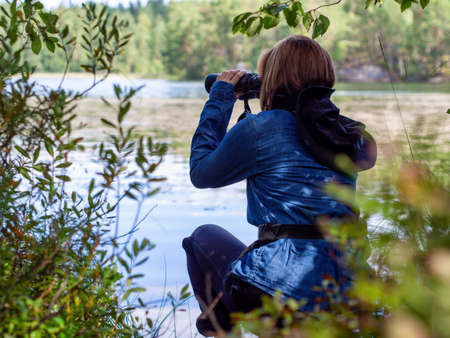 Young woman looking through binoculars at birds on the lake. Birdwatching, zoology, ecology. Research in nature, observation of animals Ornithology autumn bird migration selective focus, soft focus. photoの写真素材