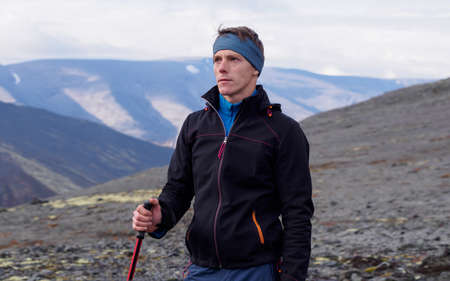 a young man with trekking poles in a bandana stands against the backdrop of mountains. photoの写真素材
