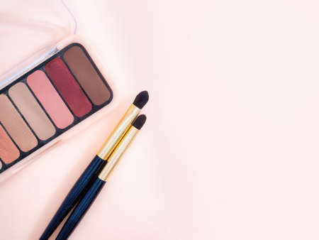 Composition with decorative makeup products golden brushes and colorful eye shadows on pastel pink background. photoの写真素材