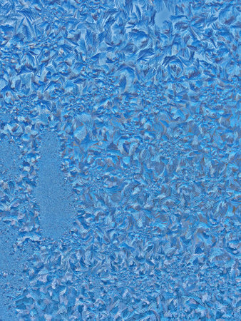 Frost delicately adorns a window pane, showing a tapestry of sparkling crystals forming intricate patterns. The cool blue tones capture the essence of winter mornings, inviting contemplation.の写真素材