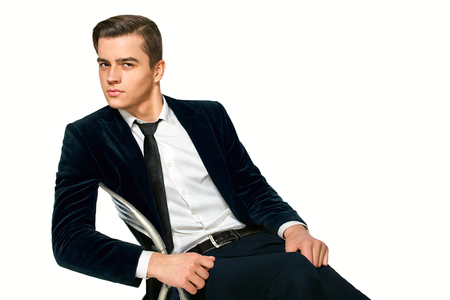 a handsome young man in a suit sitting on a chairの写真素材