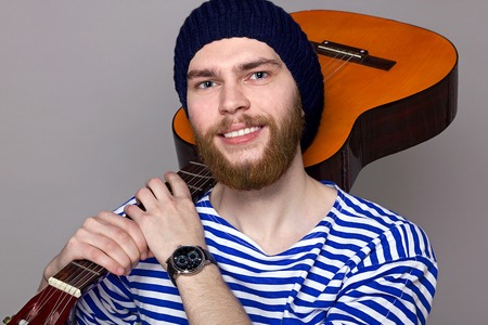 Portrait of a hipster in a striped shirt holding a guitarの写真素材