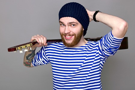 Portrait of a hipster in a striped shirt holding a guitarの写真素材