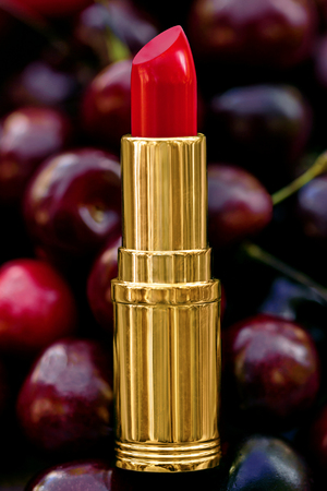 tube of red lipstick rests on a cherry