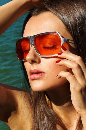 Girl in glasses with colored glasses posing against the sea close-up portraitの写真素材