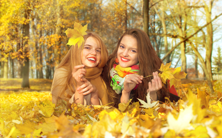 two girls lie on a leaf in an autumn parkの写真素材