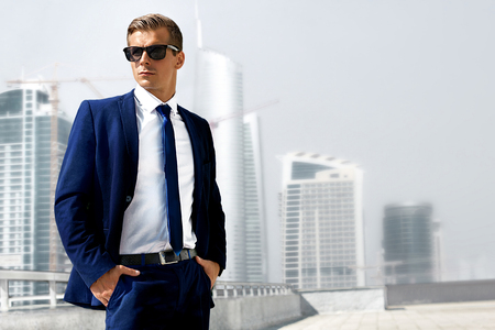 a young man in a blue suit stands against the background of the high-rise buildings being builtの写真素材