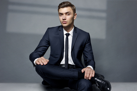 Fashionable young man sitting in the studio leg by the legの写真素材
