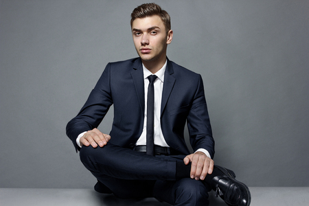 Fashionable young man sitting in the studio leg by the legの写真素材