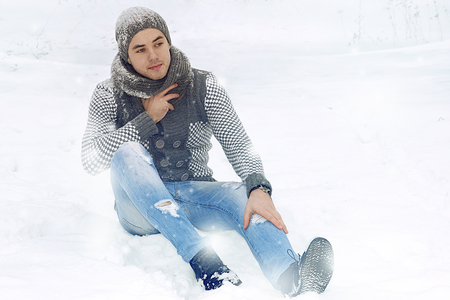 a guy in a knitted sweater and a hat sits on the snowの写真素材