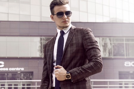 Sexy gorgeous stylish man. Sunglasses. City style. A beautiful and charming man with sunglasses outdoors. Stubble and blacks hair. Intense light. White shirt and stylish jacket.の写真素材