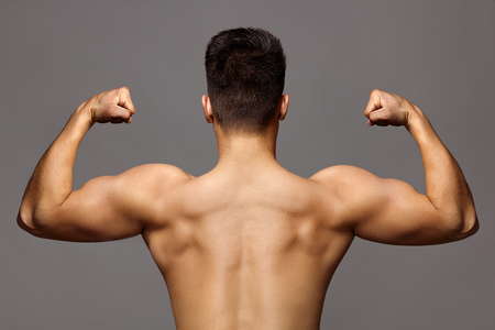 Man with muscular body and strong back of bodybuilder athlete with biceps and triceps on grey background, sport and trainingの写真素材