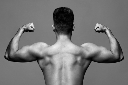 Black-and-white, monochrome photo - man with muscular body and strong back of bodybuilder athlete with biceps and triceps on grey background, sport and trainingの写真素材
