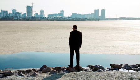 Businessman in a suit on the bank of a river on the background of the morning cityscapeの写真素材