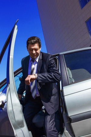 an adult, elderly, handsome man gets out of the car, looking at his watch against the background of...