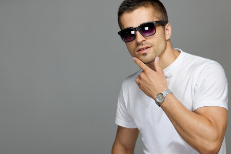 The guy in a white cotton t-shirt and sun glasses on a gray isolated background. Fashion accessory wrist watch.の写真素材