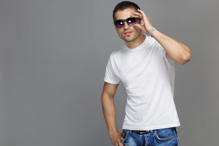The guy in a white cotton t-shirt and sun glasses on a gray isolated background. Fashion accessory wrist watch.の写真素材