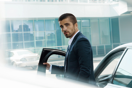Handsome brutal man near the car, against theon the background of the business center. Luxury.の写真素材