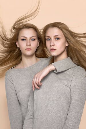 Two twin girls in a gray sweater posing in the studio on caramel pastel backgroundの写真素材