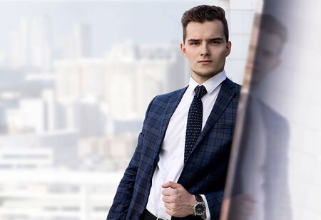 fashionably dressed man in a suit with a tie and a wristwatch on a background of the cityの写真素材